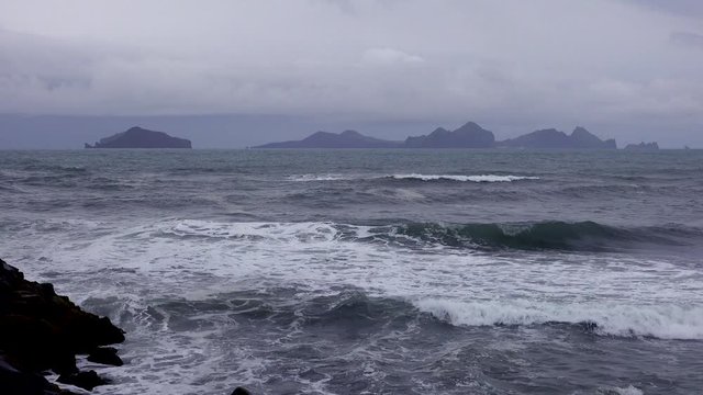Establishing shot of the Westmann Islands in Iceland with a stormy dark sea foreground.