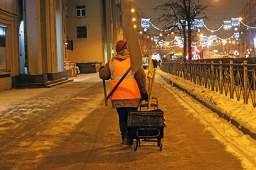 janitor with a cart and a shovel on his shoulder walking along the sidewalk