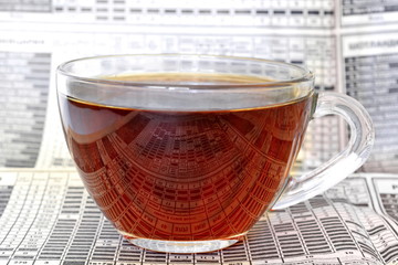 transparent glass Cup of hot strong tea on an old business newspaper with tables and figures with...