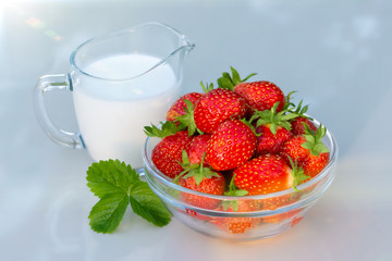 Fresh ripe strawberries in a bowl and iogurt on a white table outdoors on a summer day