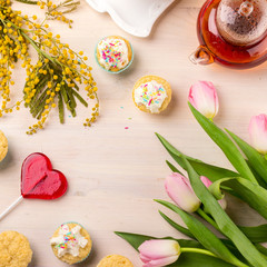 Women's day greeting card with tulips, mimosa, tea and cupcakes on wooden background.