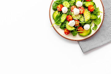 Fresh salad with mozzarella, spinach, cherry tomatoes, cucumber on plate on white background top view space for text
