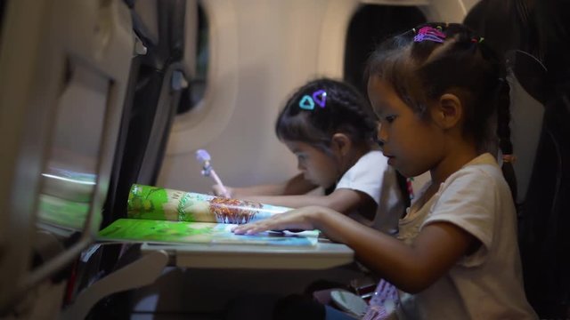 4k footage of asian little girls spending time on drawing and reading a book while traveling by plane