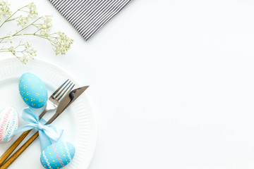 Easter table decoration in blue colors. Plate, cutlery, painted eggs and dry flower branch,...