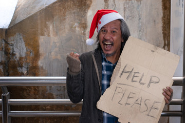 Homeless man in Santa Claus hat holding cardboard text