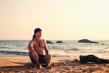 A man with a surfboard sitting on the beach against the backdrop of the sea