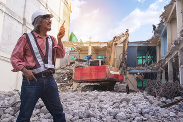Demolition control supervisor or engineer, walky talky in hand on the pile of bricks over large jackhammer construction vehicle machine