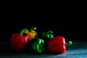Sweet peppers on the wooden plank in room which has dim light, and dark background .