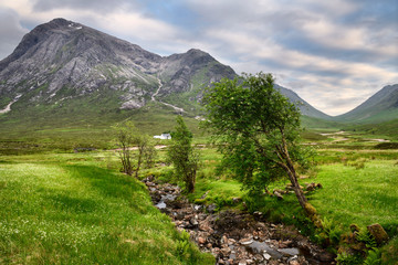 Stream to River Coupall valley with white cottage at foot of Stob Dhearg peak of Buachaille Etive Mor mountains Glen Coe Scotland UK