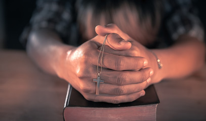 Young male praying on bible with cross in hands. christian concept.