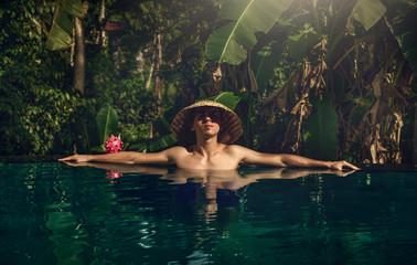 The guy in the infinity pool. Pool in the jungle. Holidays in Bali. The guy is tanning. Relax. Conical Asian hat.