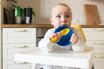 baby eat from blue plates with a yellow spoon