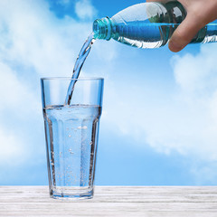 Pour sparkling  water from plastic bottle into  large glass. Bottle in  hand of  man.  Sky with clouds. Copy space.