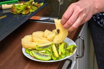 Slicing pineapples and kiwi, a plate of fruit and a hand with a knife