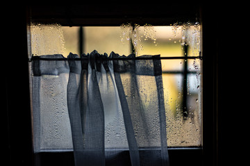 Water drops and curtains taking visibility on a window glass from indoor view