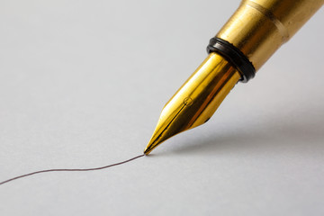 A closeup view of a gold metal nib of an old fountain pen drawing an ink line on a textured paper...