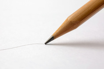 A closeup view of a wooden pencil drawing a line on a textured paper surface.