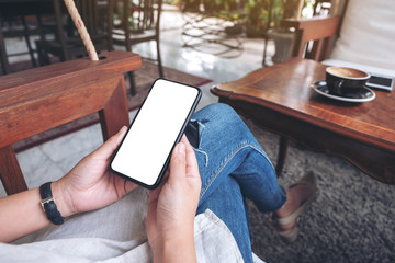 Mockup image of hands holding black mobile phone with blank white screen  while sitting in cafe