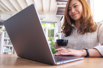 Closeup image of a beautiful asian woman using and touching on laptop touchpad while drinking coffee