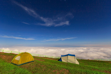 Stars shining above illuminated tent high on mountain after sunset