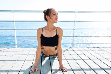 young slim athletic sports woman makes yoga exercises and stretching on seaside at sunny summer morning. front view of athletic smiling lady doing stretching against blue sea. Healthy lifestyle