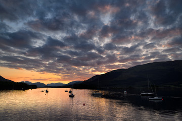 Red Sunset with clouds on Loch Leven with moored sailboats at Glencoe Boat Club and distant mountains of Scottish Highlands Scotland UK
