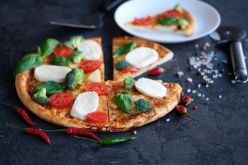 Sliced pizza with Mozzarella cheese, tomatoes, broccoli, Spices and fresh basil on black stone background. Italian pizza. One peece of pizza on a plate