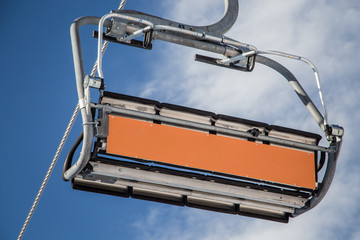 Empty ski lift with an empty orange commercial banner in front of cloudy blue sky