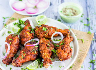 Indian Style Fried Chicken Drumsticks. Homemade Deep Fried Chicken Legs / Chicken Drumsticks in a Round Platter Served with Onion Rings, Lemon .Wedges, Cilantro and Gren Sauce.