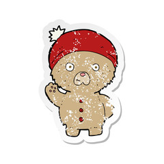 retro distressed sticker of a cartoon waving teddy bear in winter hat