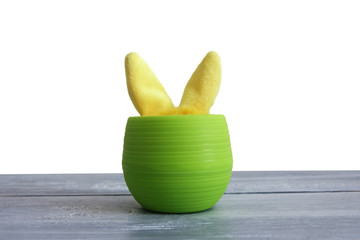 yellow plush ears of a hare stick out of a green plastic pot on a wooden background. Isolate Copy space. Easter concept..