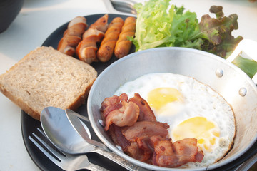 Fried eggs, bacon and sausage on pan, sliced bread and vegetable on a plate. concept breakfast.