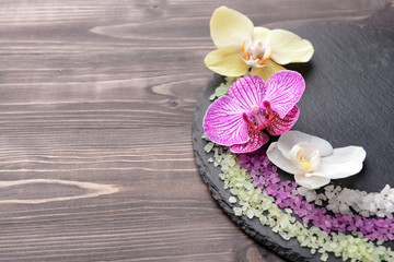 Slate plate with beautiful orchid flowers and sea salt on wooden background