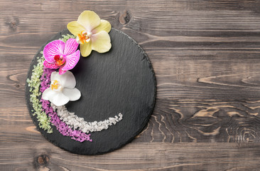 Slate plate with beautiful orchid flowers and sea salt on wooden background
