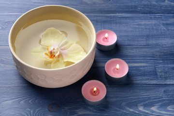 Bowl with water, orchid flower and candles on wooden background