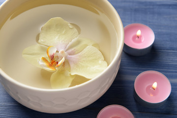 Bowl with water, orchid flower and candles on wooden background, closeup