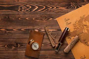 Spyglass, scrolls, compass, notebook and world map on wooden background. Travel concept