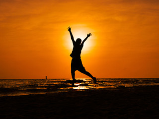 Silhouette boy jumping and raising hands on the beach in sun rise.