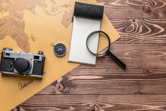 Notebook, magnifier, compass, photo camera and world map on wooden background. Travel concept