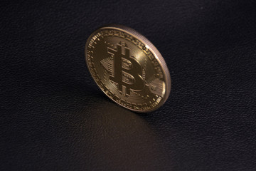 gold coin bitcoin stands upright on black leather