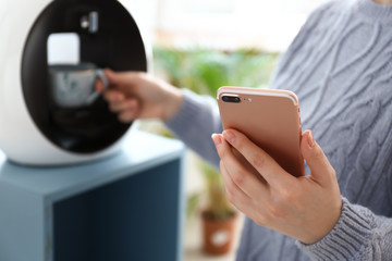 Young woman with mobile phone making coffee indoors