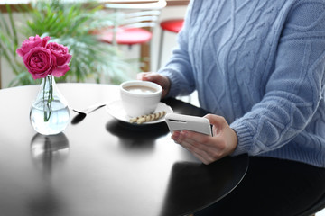 Young woman with mobile phone drinking coffee at table
