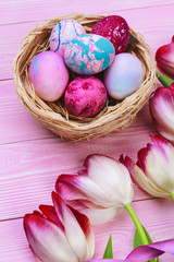 Fototapeta na wymiar Easter background with colorful eggs and tulips over pink wood. Top view with copy space
