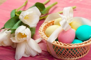 easter, holidays, tradition and object concept - close up of colored eggs and tulip flowers over wooden boards background