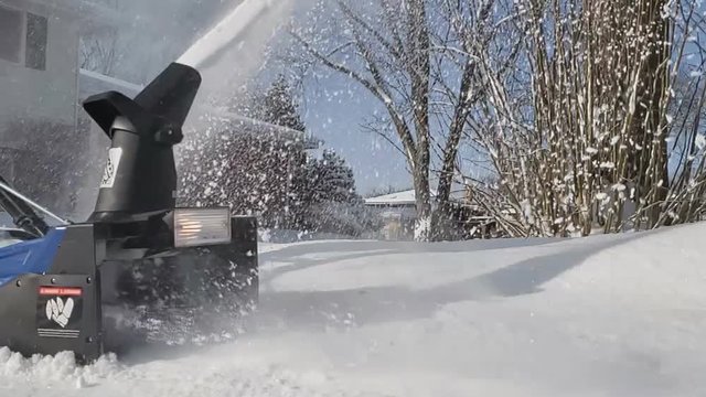Close up and super slow motion of electric snowblower machine being used for snow removal from driveway. Close up of spinning auger picking up a lot of snow.