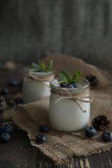 Fresh natural homemade organic yogurt with blueberries, in a glass jar on a wooden background