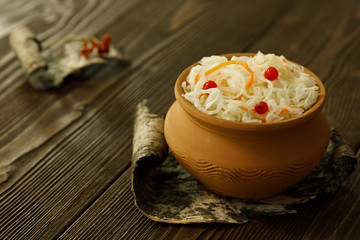 Home sauerkraut with carrots in a clay pot on a wooden table.