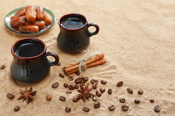 Cups of coffee on a sandy background with coffee beans and cinnamon