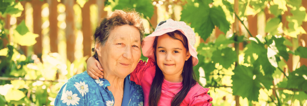 Great-grandmother And Granddaughter Standing In Flower Field In Sunlight