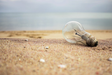 Fototapeta na wymiar Old light bulb on the sand. Garbage on the beach. Environmental pollution. Save the Planet. Ecological problem. Energy or inspiration concept. Nature theme.